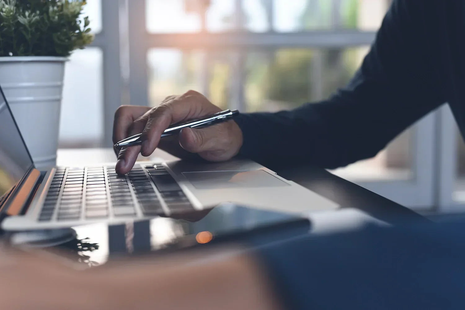 Main avec un stylo qui tape sur un clavier d'ordinateur