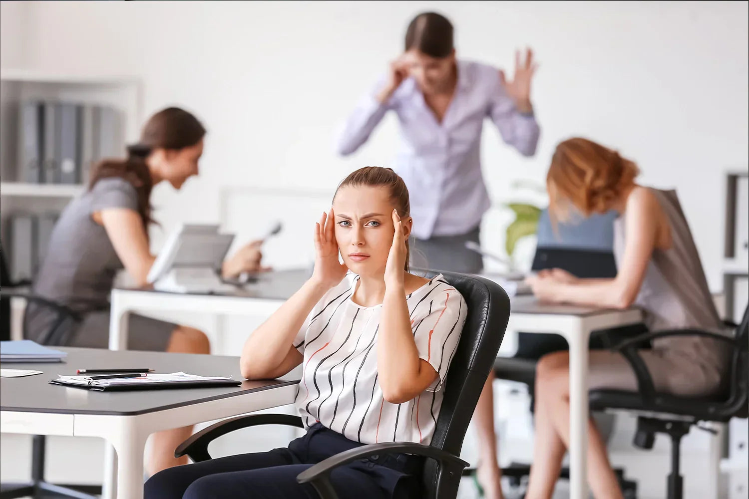 Femme assis sur sa chaise de bureau dans une ^pièce très éclairée, elle semble être dérangé par le bruit autour d'elle