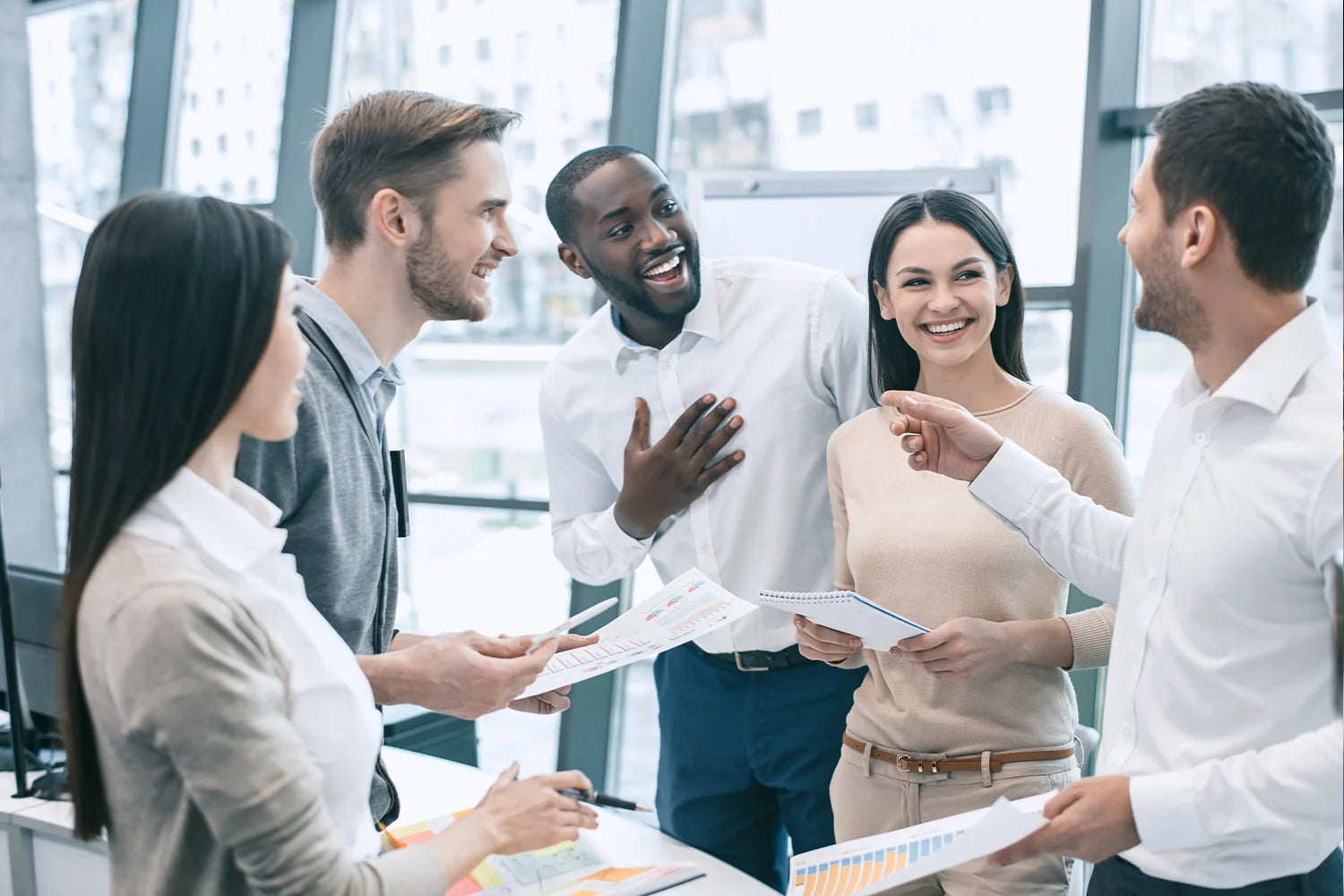 5 hommes et femmes en train de discuter joyeusement debout lord d'une réunion