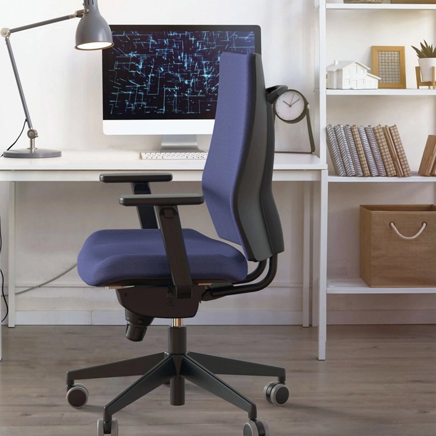 Espace de travail à la maison composé d'un bureau avec un ordinateur, un lampe et une horloge et en premier plan un siège ergonomique bleu avec des accoudoirs