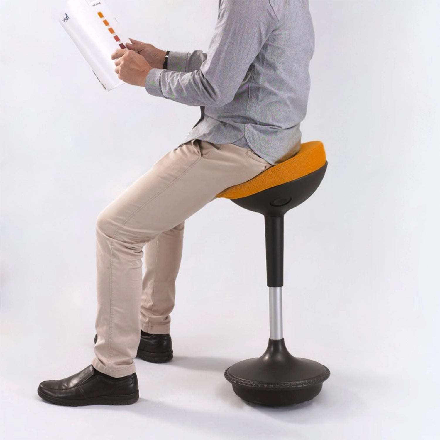 Homme feuilletant un magazine, confortablement installé sur le tabouret ergonomique orange